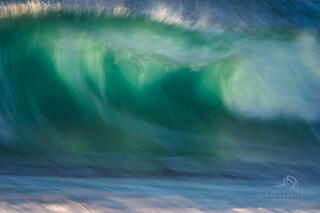 Abstract wave photography image shows swirls of white and blue as the wave just about breaks before it hits the shore.