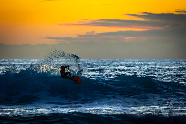 A surfer finds rhythm with the waves at sunset and manages a graceful cutback with a fiery orange sky as the backdrop.